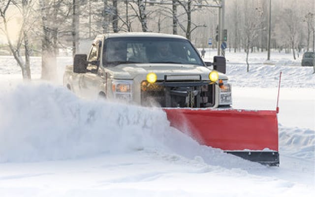 A large white truck with a red plow moves snow